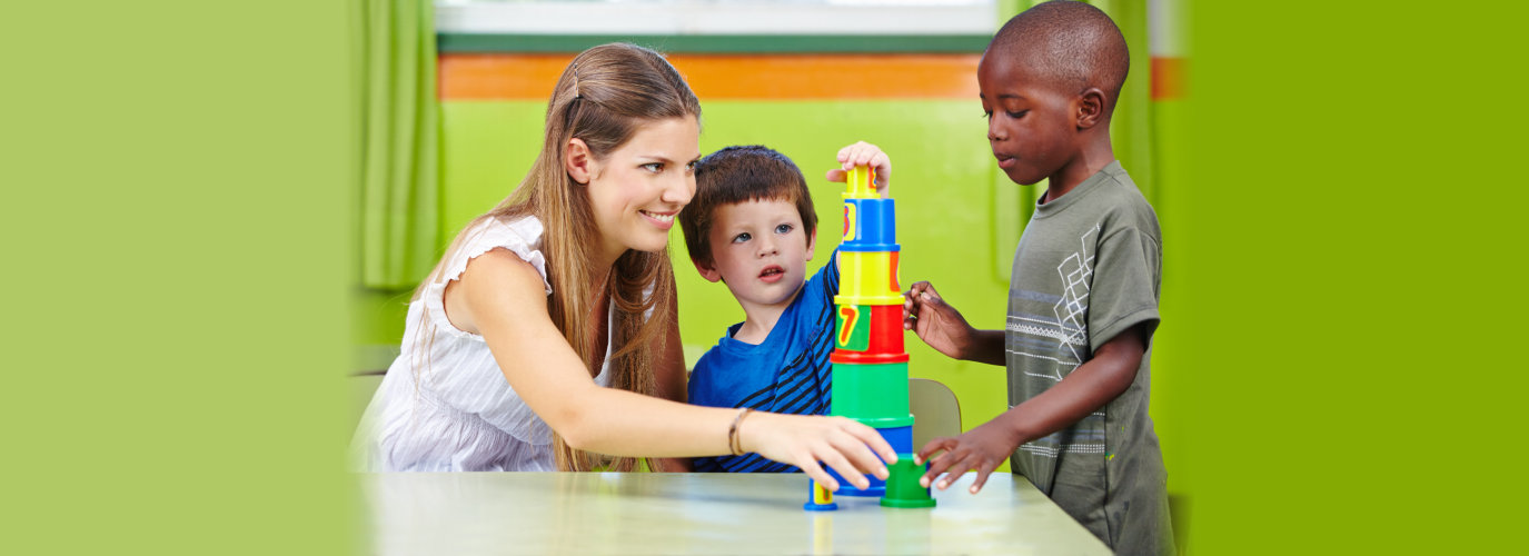 Educator plays with boys in kindergarten and builds a tower out of building blocks